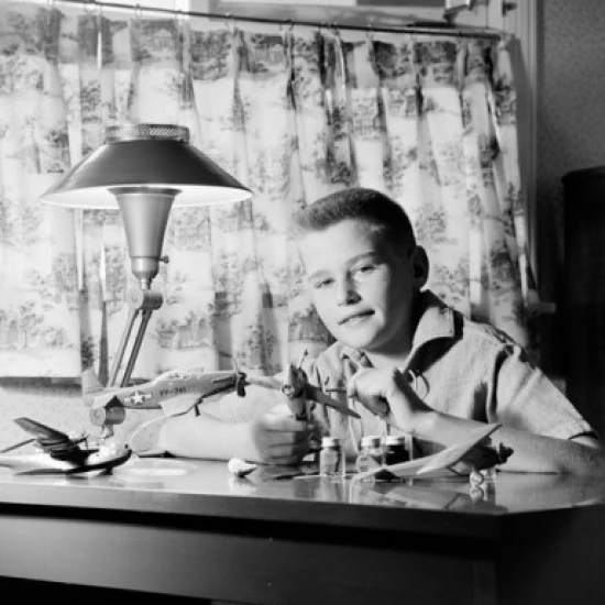 Boy sitting at desk and making model plane Poster Print (18 x 24)