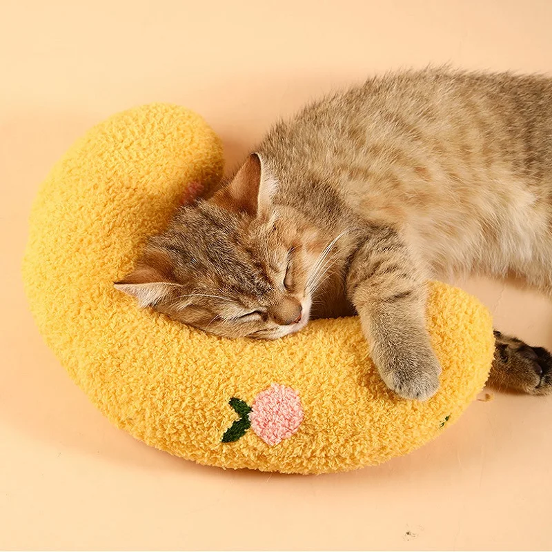 A tabby cat is sleeping on a yellow, crescent-shaped Cozy Pet Pillow for Cats and Small Dogs made of soft & cozy material from The Stuff Box, with a small pink embroidered detail.