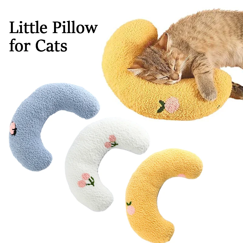 A cat is sleeping on a small, orange, crescent-shaped pillow made of soft & cozy material. Three similar pillows in blue, white, and yellow are displayed below. The text reads: "Cozy Pet Pillow for Cats and Small Dogs - Calming & Anxious Relief by The Stuff Box.