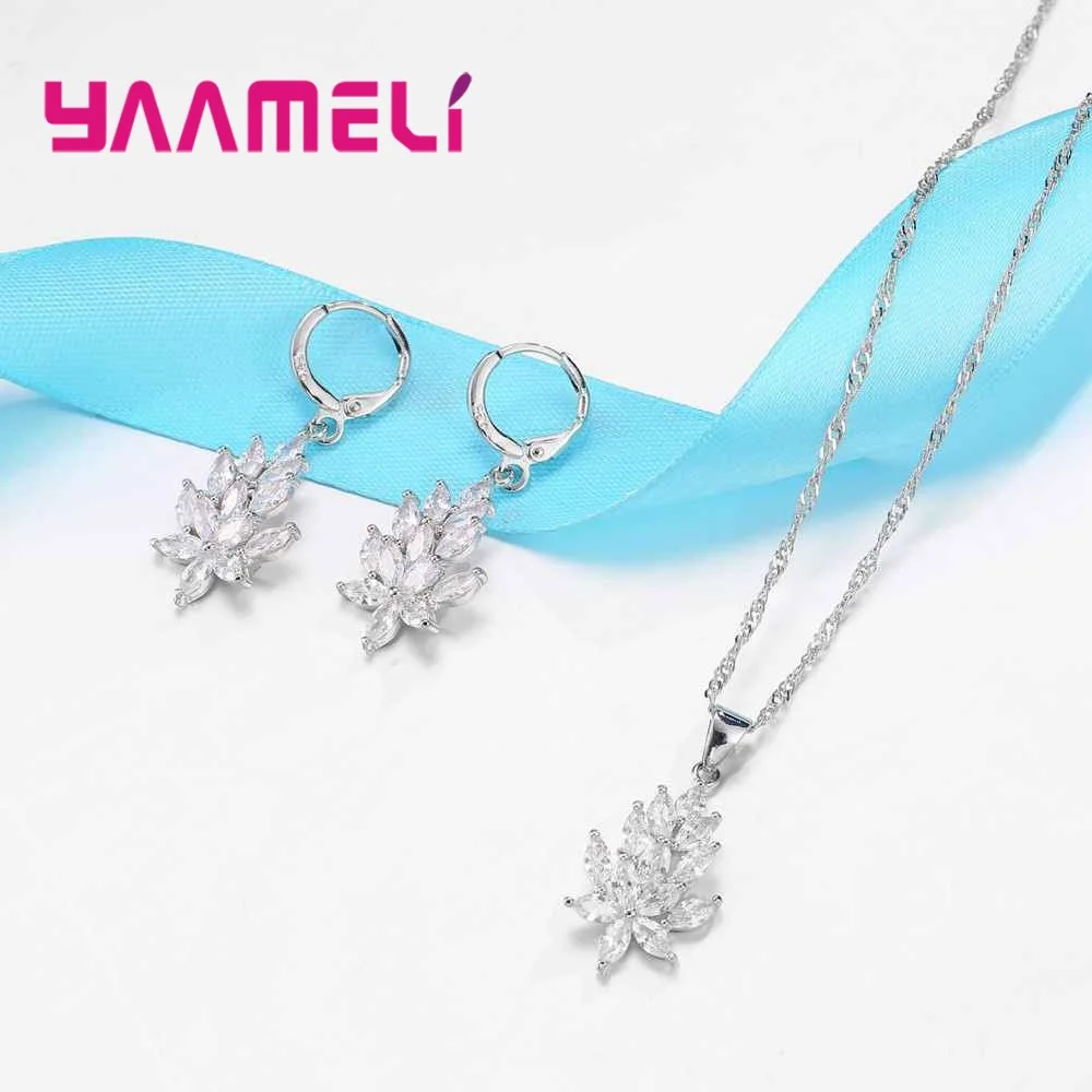 Conjunto de joyería de hoja de cristal plateado que incluye un collar de colgante con forma de flor de loto de plata con acentos de cristal transparente y una cadena trenzada, acompañado de pendientes tipo aro a juego.