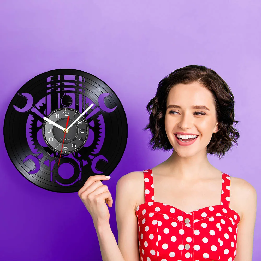 A woman in a red polka dot dress smiles while pointing at the Black Record Wall Clock, showcasing its unique design that adds a mechanical and rustic vibe against the purple background.
