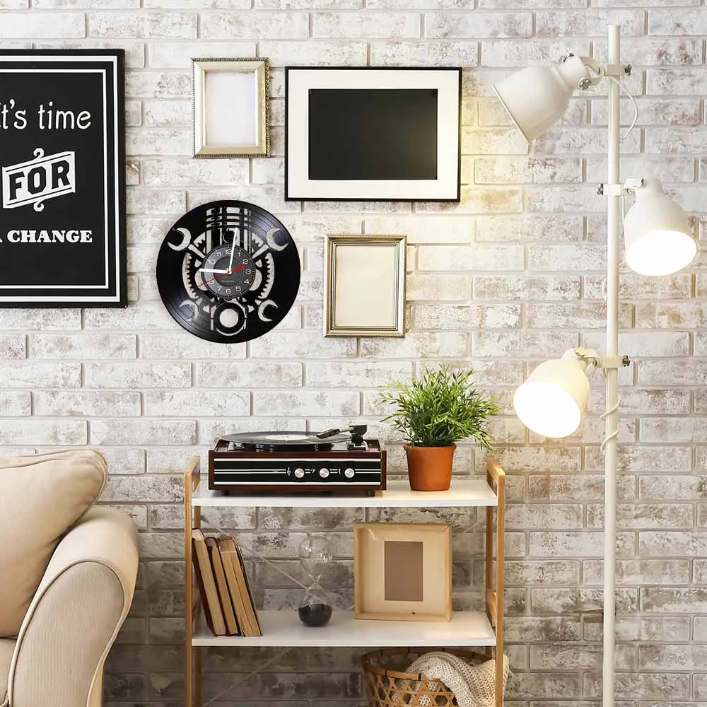 A cozy living room with a white brick wall, featuring a Black Record Wall Clock, a turntable on a small shelf, framed pictures, a potted plant, and a standing lamp with three bulbs.