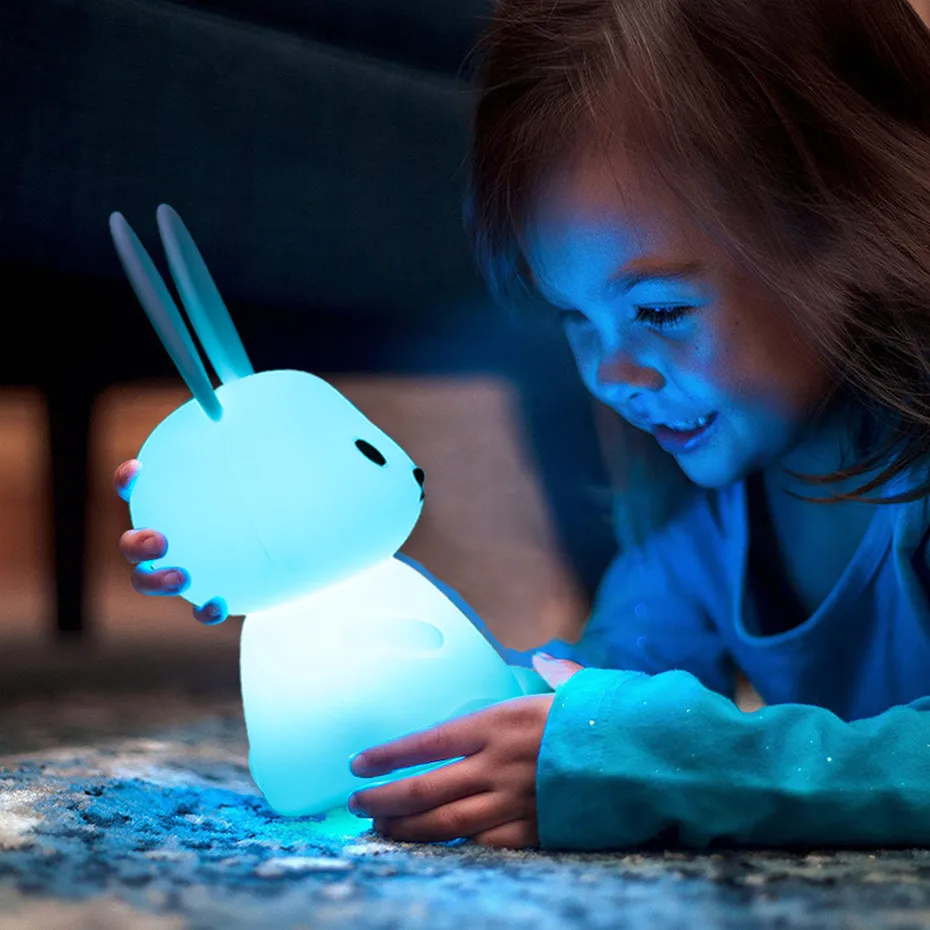 A little girl playing with a blue bunny toy that has color-changing LED lights.