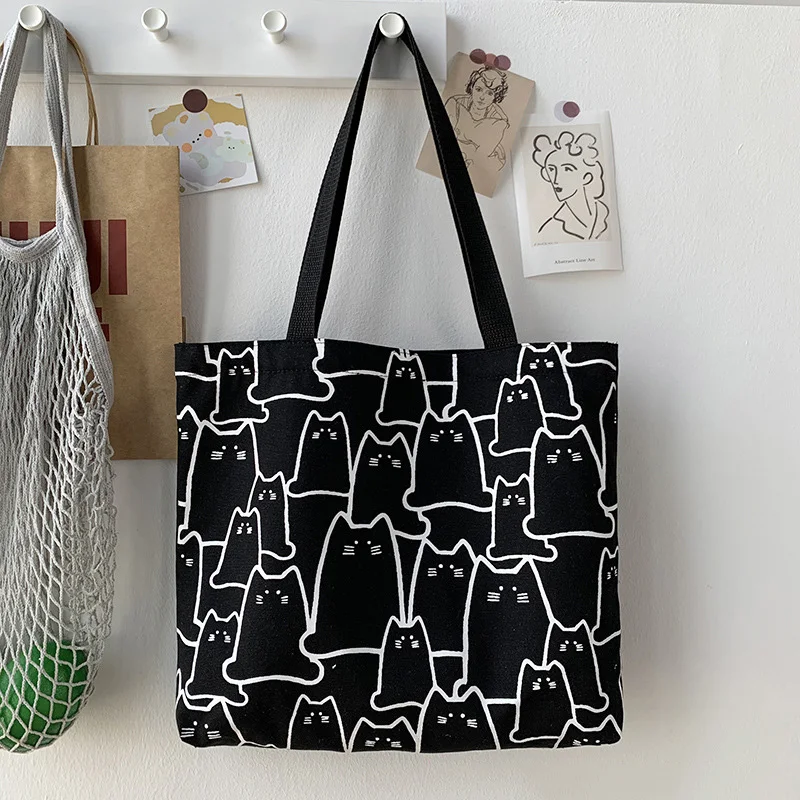 a black color cat tote bag hanging on the wall printed with many cute cats