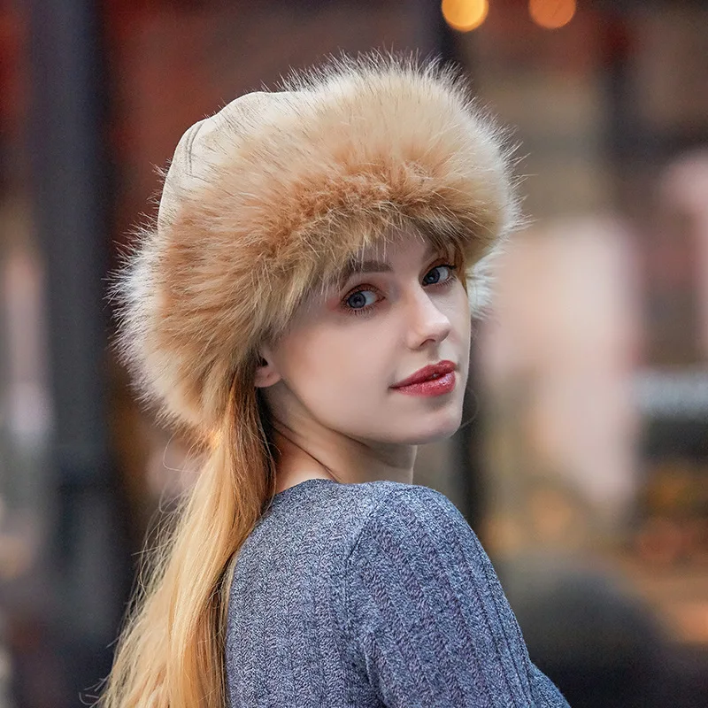 Une jeune femme, se tient de trois quart et porte un haut gris, et un chapeau russe à fourrure beige