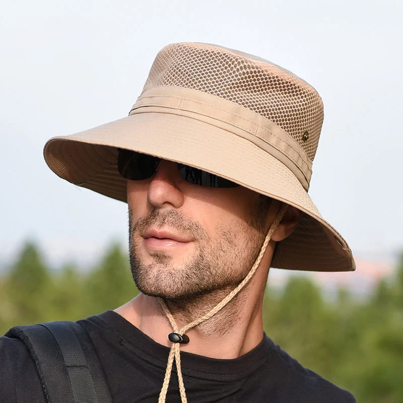 Homme dans la nature, portant un chapeau bob semi-ajouré beige avec le cordon sous le cou ajusté. On ne voit que sa tête et le début de ses épaules, il porte un t-shirt noir