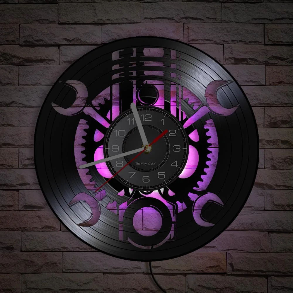 The Black Record Wall Clock, showcasing a rustic industrial design with a vinyl record and mechanical gears, is elegantly mounted on a stone wall and illuminated by a vibrant purple backlight.