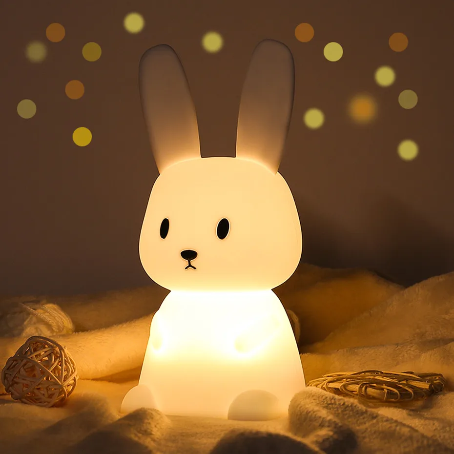 A Bunny Touch Lamp, featuring color-changing LED lights and offering seven colors, sits on top of a cozy blanket.