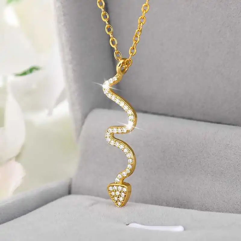 A stylish jewelry piece, the Snake Pendant features a wavy gold design encrusted with small diamonds, elegantly presented on a gray velvet display.