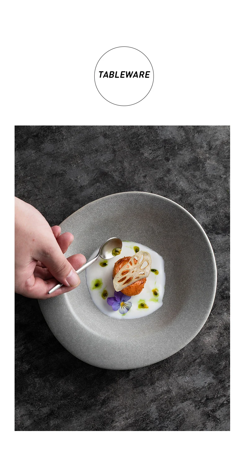 Hand placing a spoon over a grey ceramic bowl with a plated dish—lotus root chip, edible flower and green sauce dots—on a dark stone surface.
