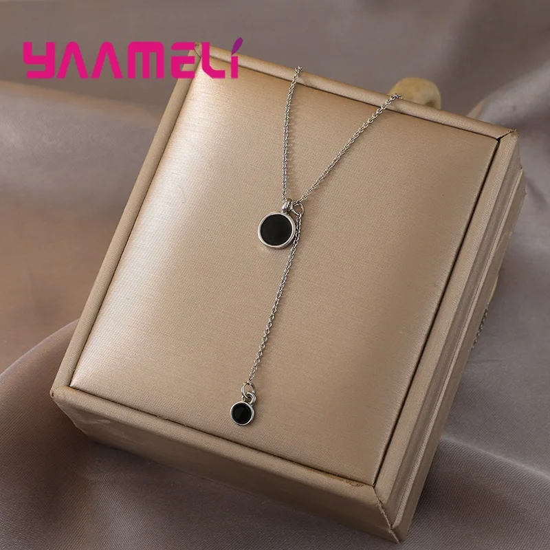 Collar de cadena de plata de ley con dos dijes circulares negros mostrados en una caja de regalo color beige.