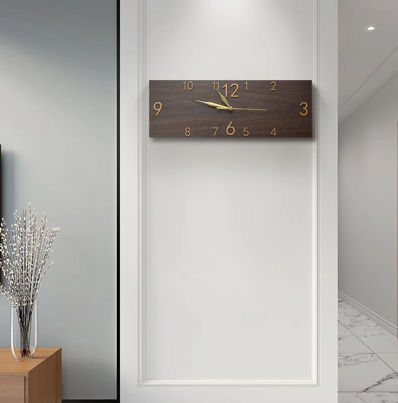 A contemporary rectangle wall clock with wooden backing and gold-tone numerals mounted on a white wall in a minimalist interior acts as an elegant accessory.