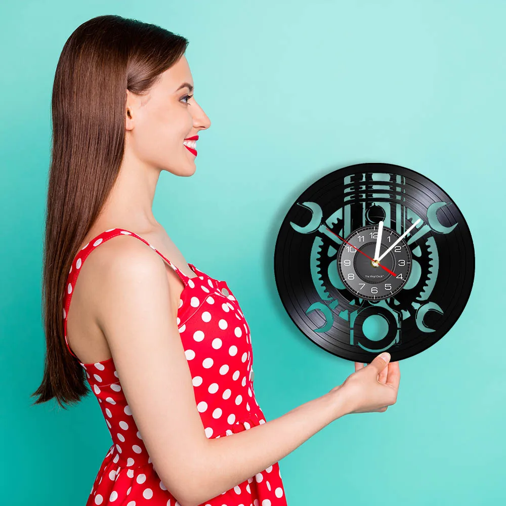 A woman in a red polka dot dress holds the Black Record Wall Clock, showcasing its unique design and mechanical vibe against a teal background.