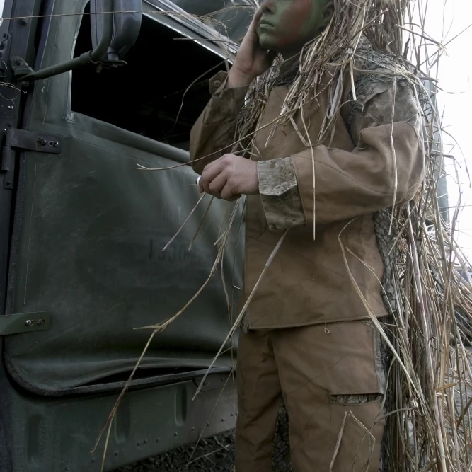 A scout observer applies camouflage paint after donning his homemade ghillie suit Poster Print (11 x 17)