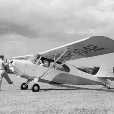man rotating the propeller of a private plane with a woman sitting