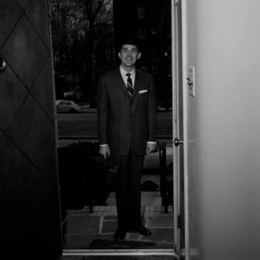 Man wearing suit standing in doorway of house Poster Print (18 x 24)
