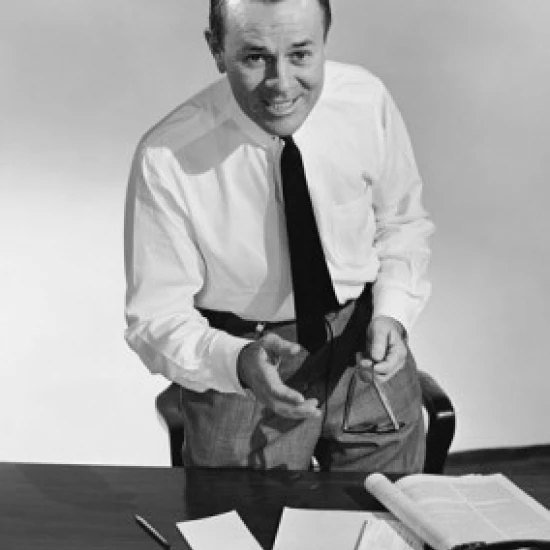 Businessman standing at a desk in an office and smiling Poster Print (18 x 24)