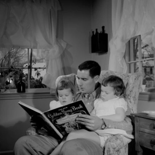 Father reading to daughters in living room Poster Print (18 x 24)