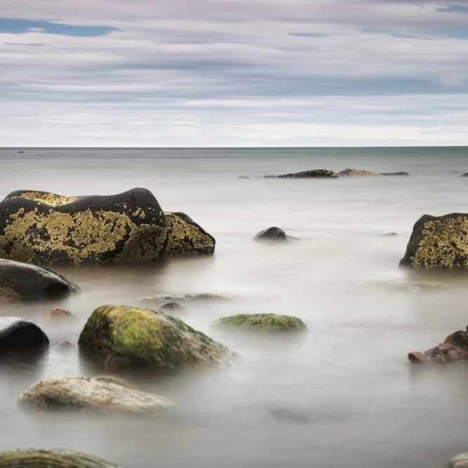 Large rocks sitting in the water Poster Print (19 x 12)