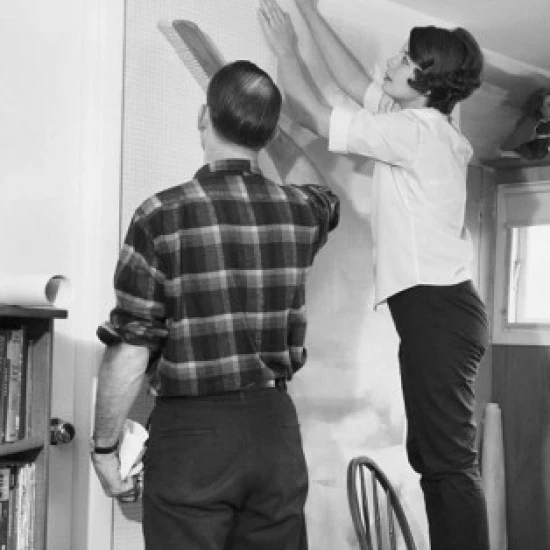 Mid adult couple applying wallpaper in a room Poster Print (24 x 36)