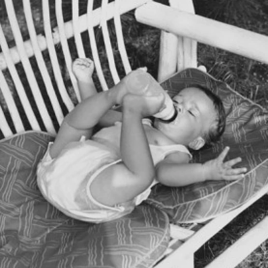 High angle view of a baby lying on a couch and drinking milk from a bottle Poster Print (18 x 24)