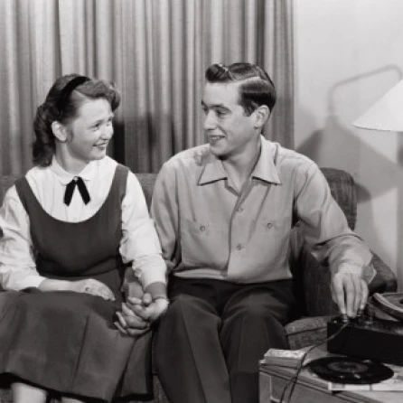 Young couple sitting on sofa near record player Poster Print (24 x 36)