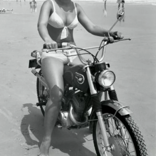Young woman riding motorcycle on beach Poster Print (18 x 24)