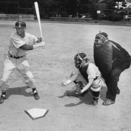 Baseball player swinging a baseball bat with a baseball catcher and a baseball umpire beside him Poster Print (18 x 24)