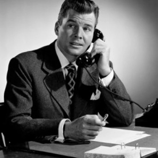 Mid adult man sitting at desk talking on phone Poster Print (18 x 24)