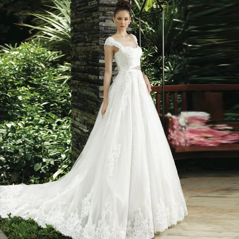 A model in a long-sleeved sheer boat neck wedding dress with a beaded belt and full skirt