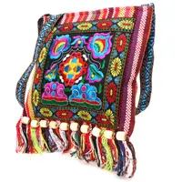 Sac à main de style rétro, hippie, coloré, à bandoulière, avec des franges colorées en bas. La bandoulière a un motif géométrique coloré. Le sac a un beau motif multicolore.