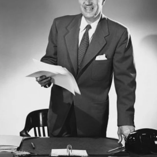 Businessman standing at a desk and holding documents in an office Poster Print (18 x 24)