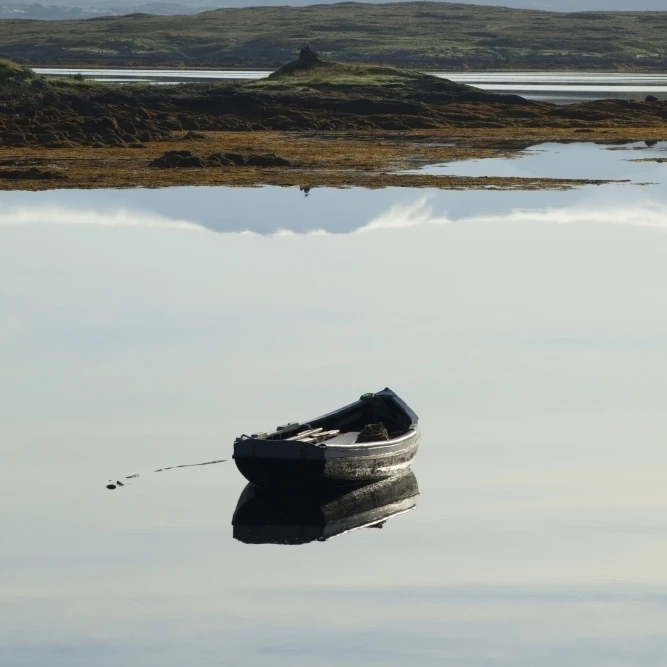 A rowboat sits in a tranquil lake with hills in the background near roundstone;County galway ireland Print (12 x 19)