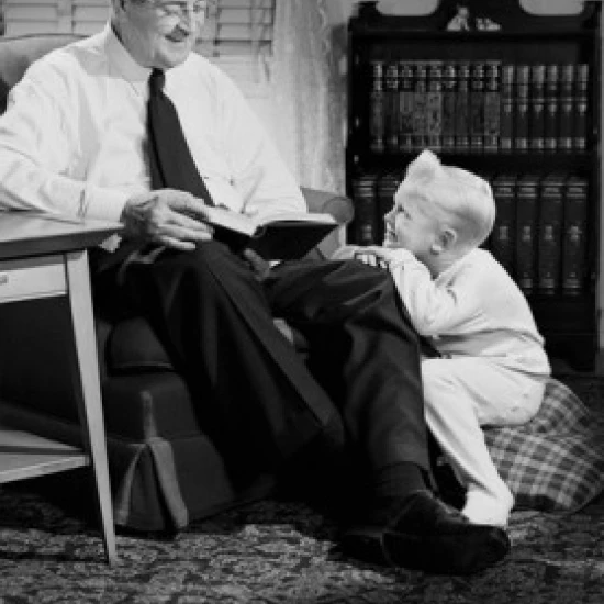 Grandfather reading to grandson in living room Poster Print (24 x 36)