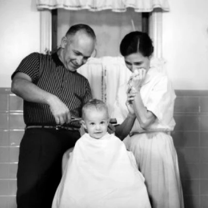 Father cutting son's hair while mother watching Poster Print (18 x 24)
