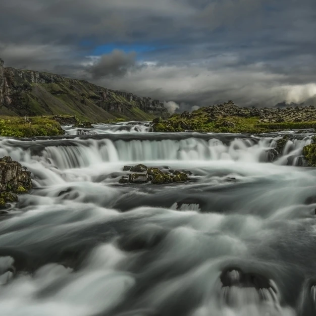Water flowing over a rugged landscape under a cloudy sky; Iceland Poster Print (38 x 24)