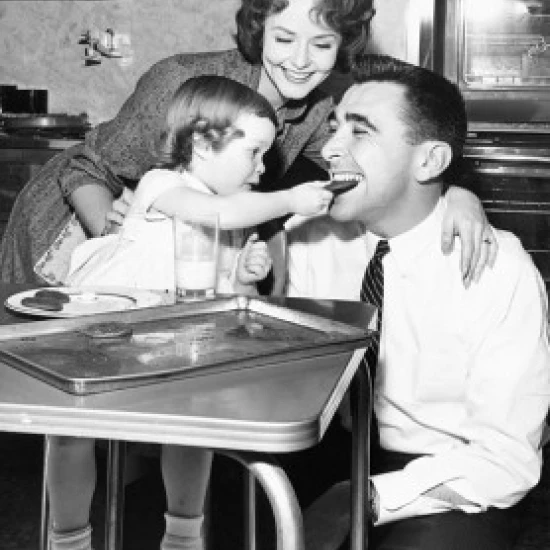 Girl feeding a cookie to her father with her mother looking at them Poster Print (24 x 36)