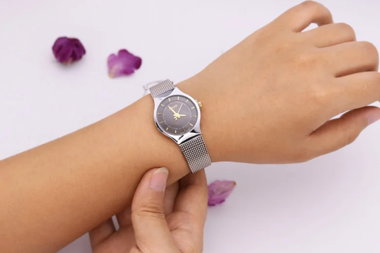 õhuke hõbedane käekell naise randmel, taustal lillad kroonlehed