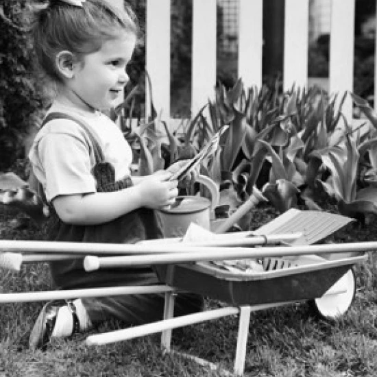Side profile of a girl holding seed packets in a garden and smiling Poster Print (18 x 24)
