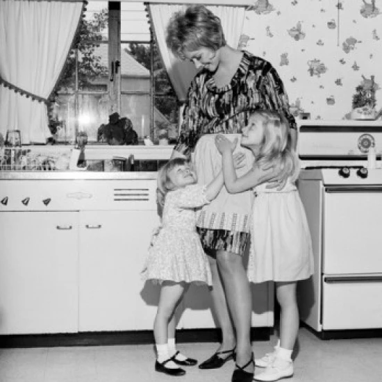Mother embracing daughters in kitchen Poster Print (24 x 36)