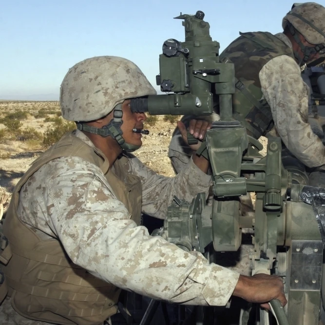 A cannoneer looks through sights of M777 Lightweight Howitzer as another crewman inserts bag of gunpowder barrel (33x22)