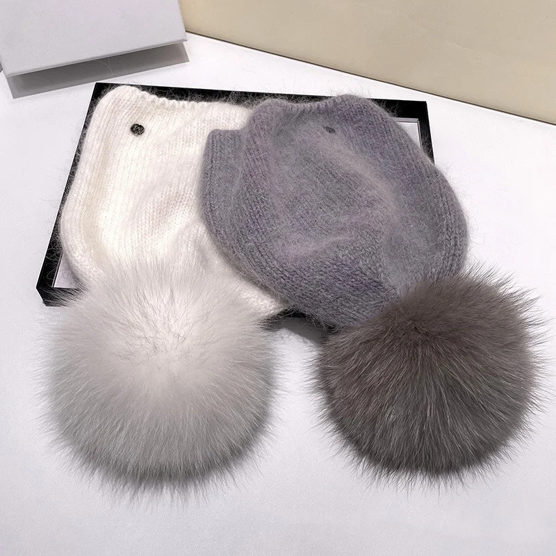 un bonnet blanc avec un pompon en fourrure blanc et un bonnet gris avec un pompon en fourrure grise