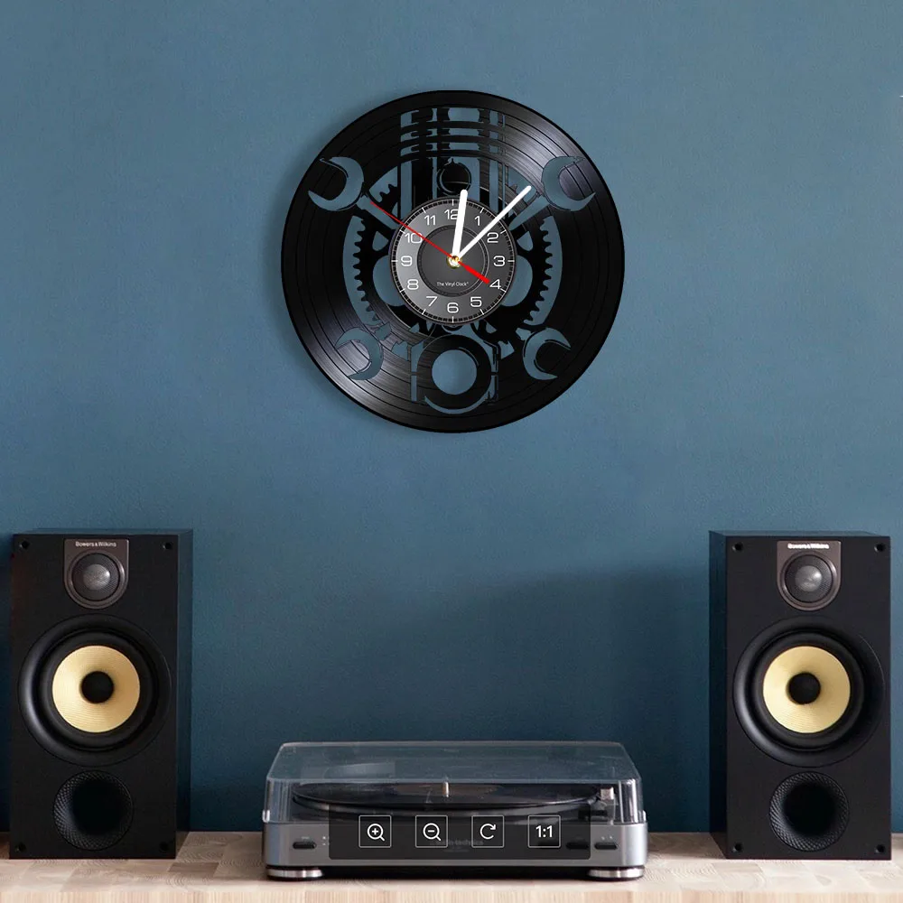 The Black Record Wall Clock, exuding rustic industrial charm with its clock hands and numbers, is mounted on a blue wall above a stereo system equipped with a record player and two speakers.