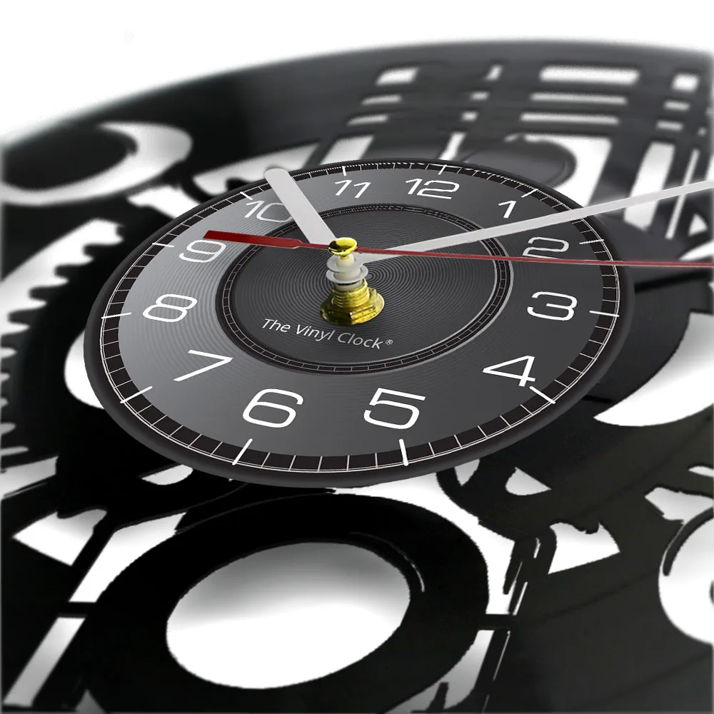 Close-up of a Black Record Wall Clock featuring white numbers and silver and red hands, with "The Vinyl Clock" inscribed on the face. It embodies a rustic industrial wall clock aesthetic, set against a blurred background with a gear-like design.