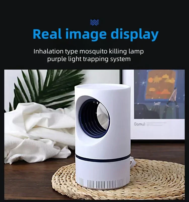 A white, cylindrical NEW Indoor Electric Mosquito Trap is positioned on a woven mat. It features a USB power supply and adapter suction fan, complemented by its purple light trapping system. A plant and framed picture are visible in the background. The text reads: "Real image display, Inhalation type mosquito killer lamp, purple light trapping system.