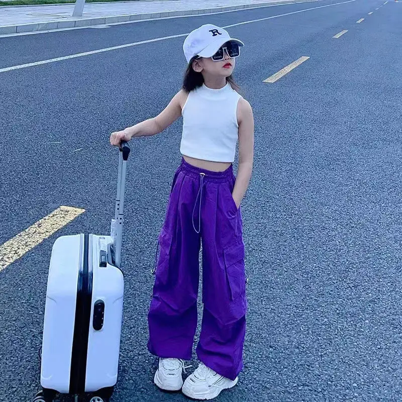 Teen girl posing in high-waisted cargo joggers with a vintage streetwear look, standing against a graffiti wall purple