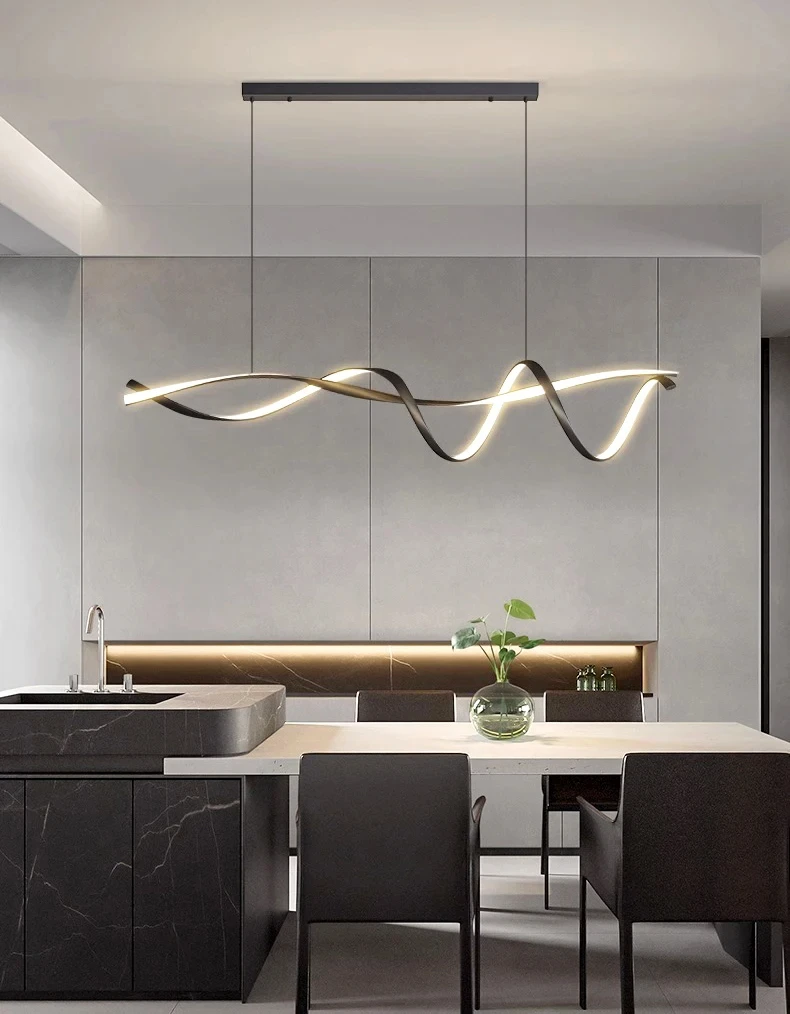 Modern kitchen featuring a Stylish Pendant Light, gray cabinetry, a dark island, and a dining table with black chairs. A green plant in a glass vase on the table adds nature-inspired design.