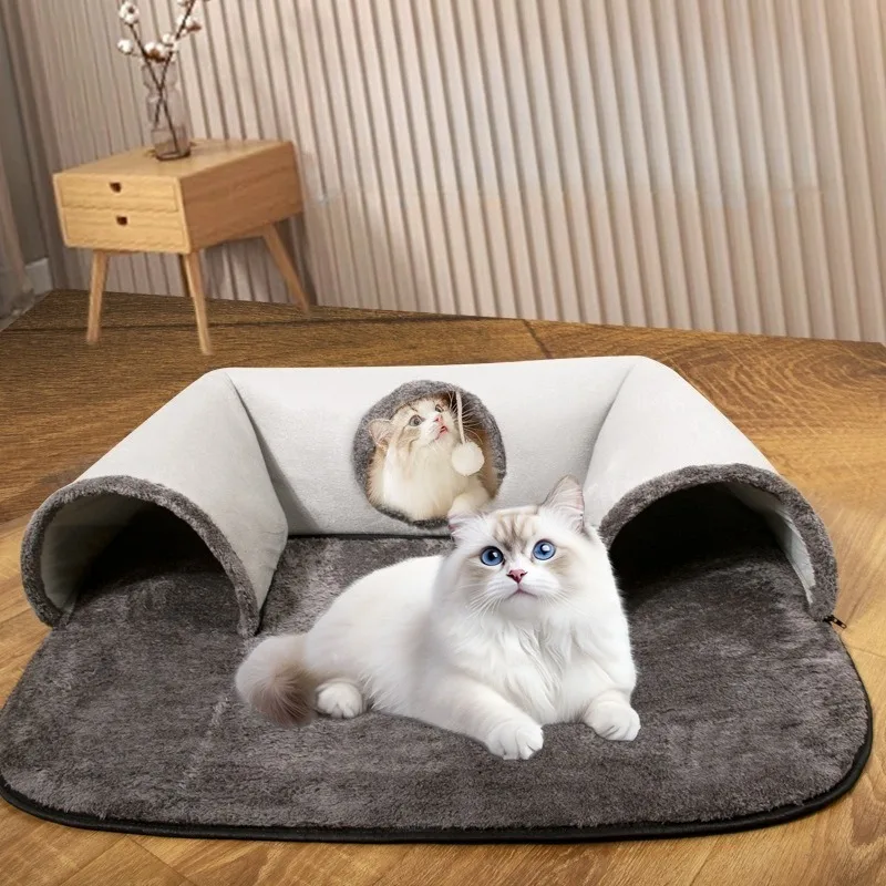 Two fluffy white cats on a gray mat; one lies down as the other peeks from a KittyNook Cat Co. U-shaped Tunnel.
