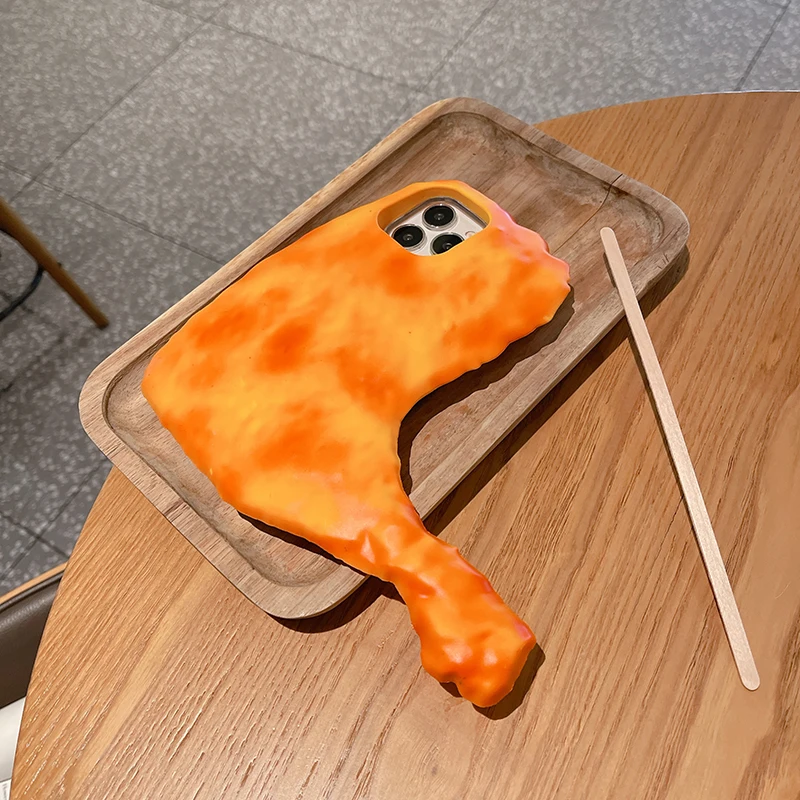 A wooden tray on a table holds a smartphone encased in the creative Chicken Drumstick iPhone Case, accompanied by a wooden stick.