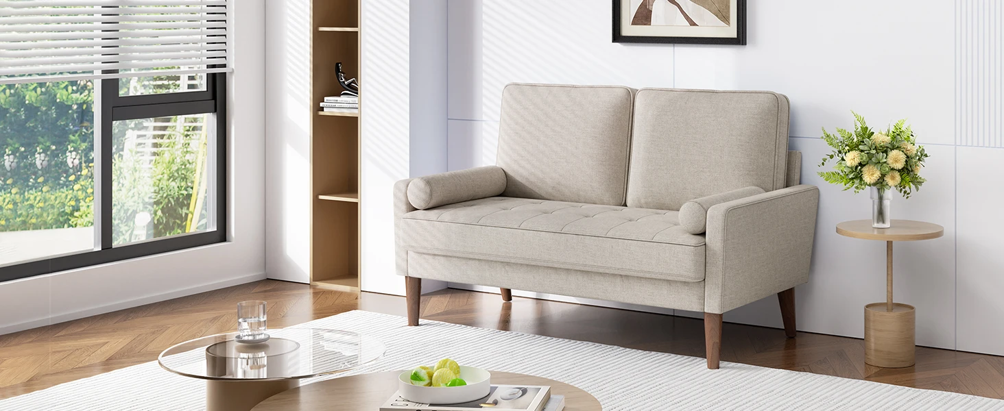 Modern two-seater loveseat in light beige upholstery with tufted cushions and wooden legs, positioned in a bright living room setting.